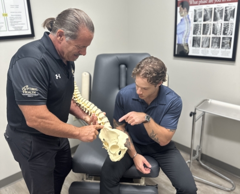 Doctor speaking with model of spine in hand speaking with patient before chiropractic adjustment